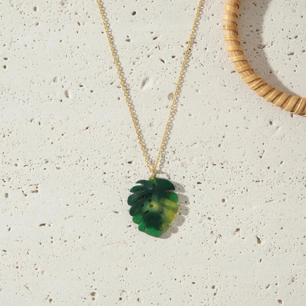 Necklace with a green leaf pendant on a textured beige surface