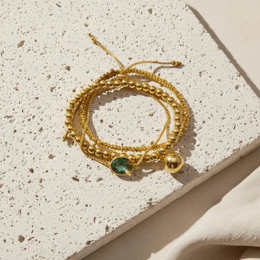 Gold bracelet with a green gemstone on a textured beige surface