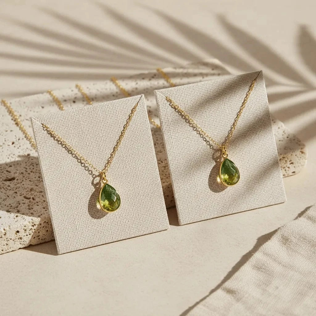 Gold necklaces with green teardrop pendants on beige display cards.