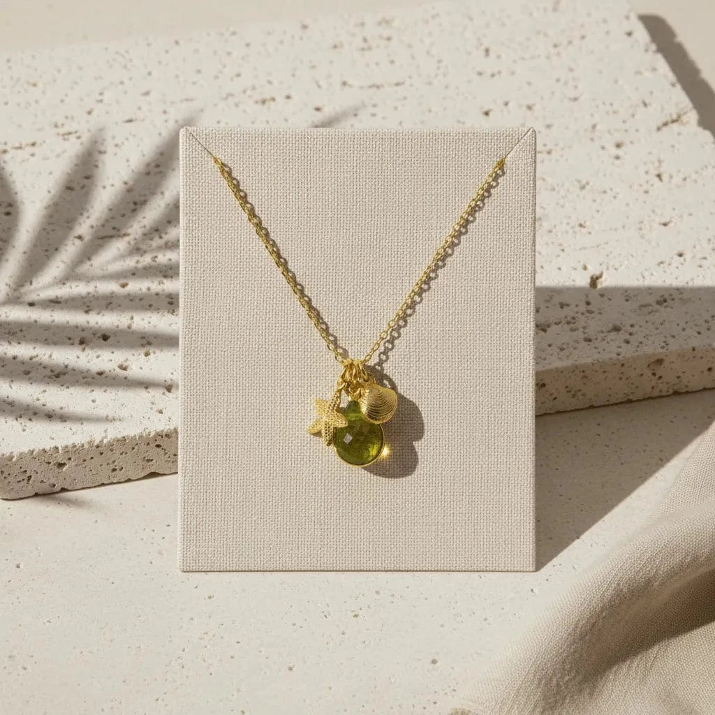Gold necklace with green pendant on a beige card against a textured beige background