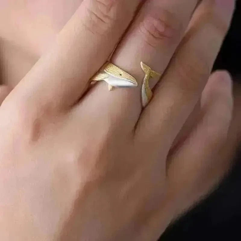 Close-up of a hand wearing a gold ring with a whale design.