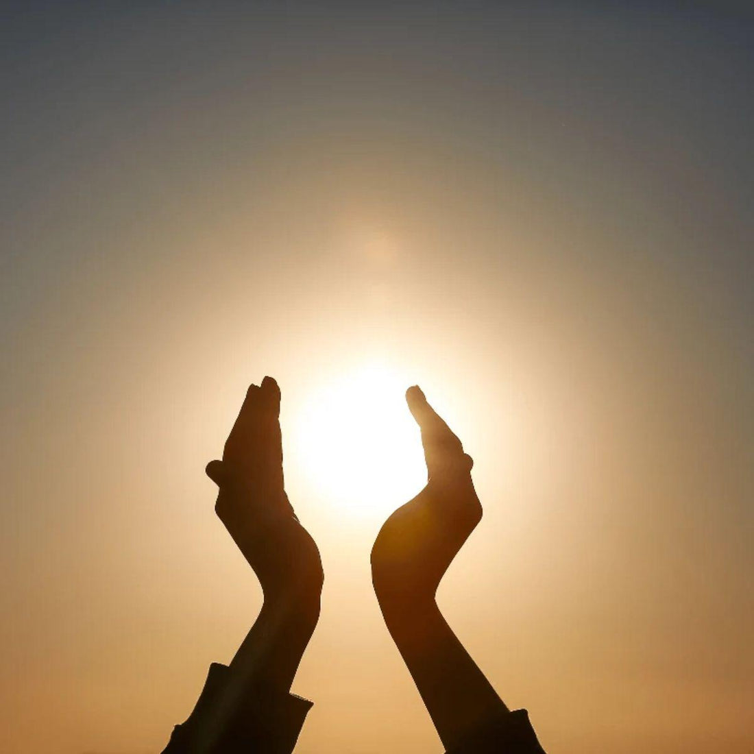Hands holding a low setting sun — winter solstice rituals and intention setting for the longest night