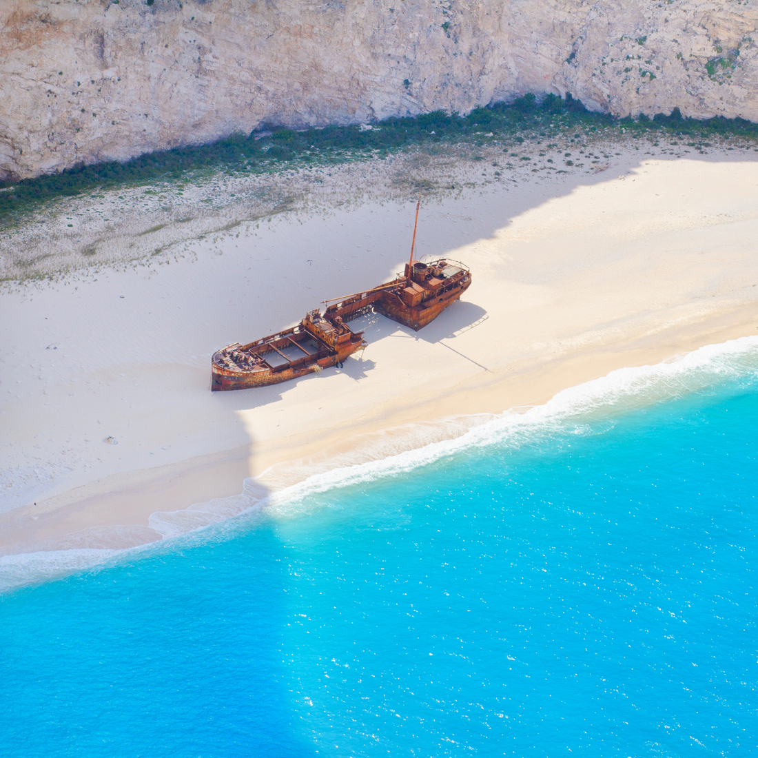 Navagio Shipwreck Beach on Zakynthos, Greece — the rusted hull on white pebbles below sheer cliffs, surrounded by vivid Capri blue water