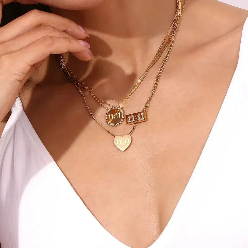 Gold necklaces with heart and rectangular pendants on a person wearing a white top.