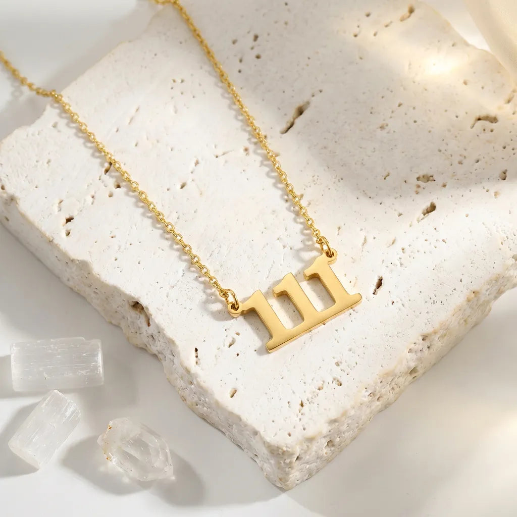111 angel number Gold necklace with a three-bar design on a textured white surface