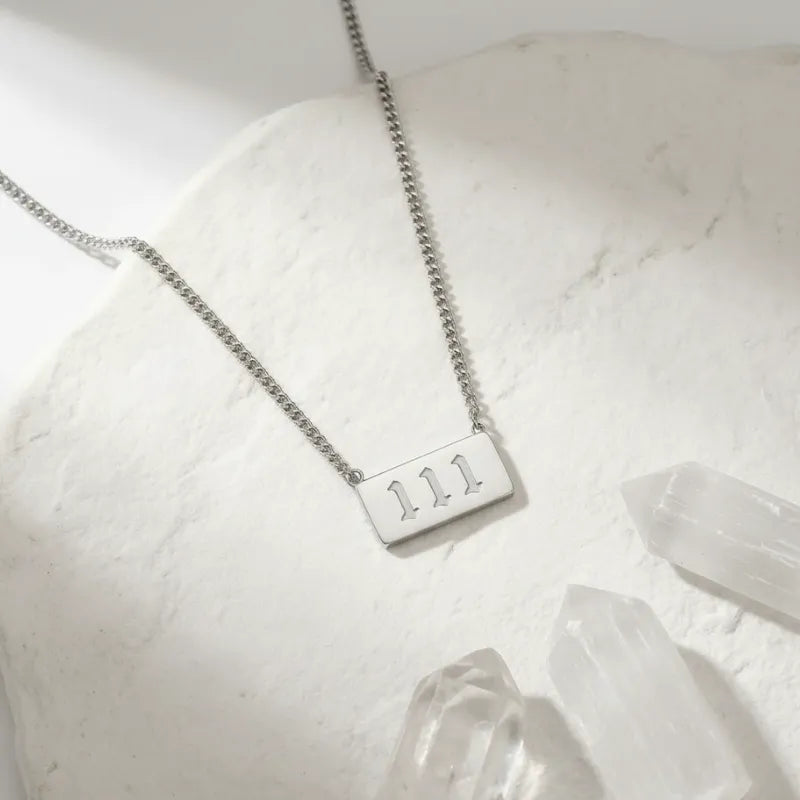 Silver necklace with engraved '111' on a white surface with crystals.