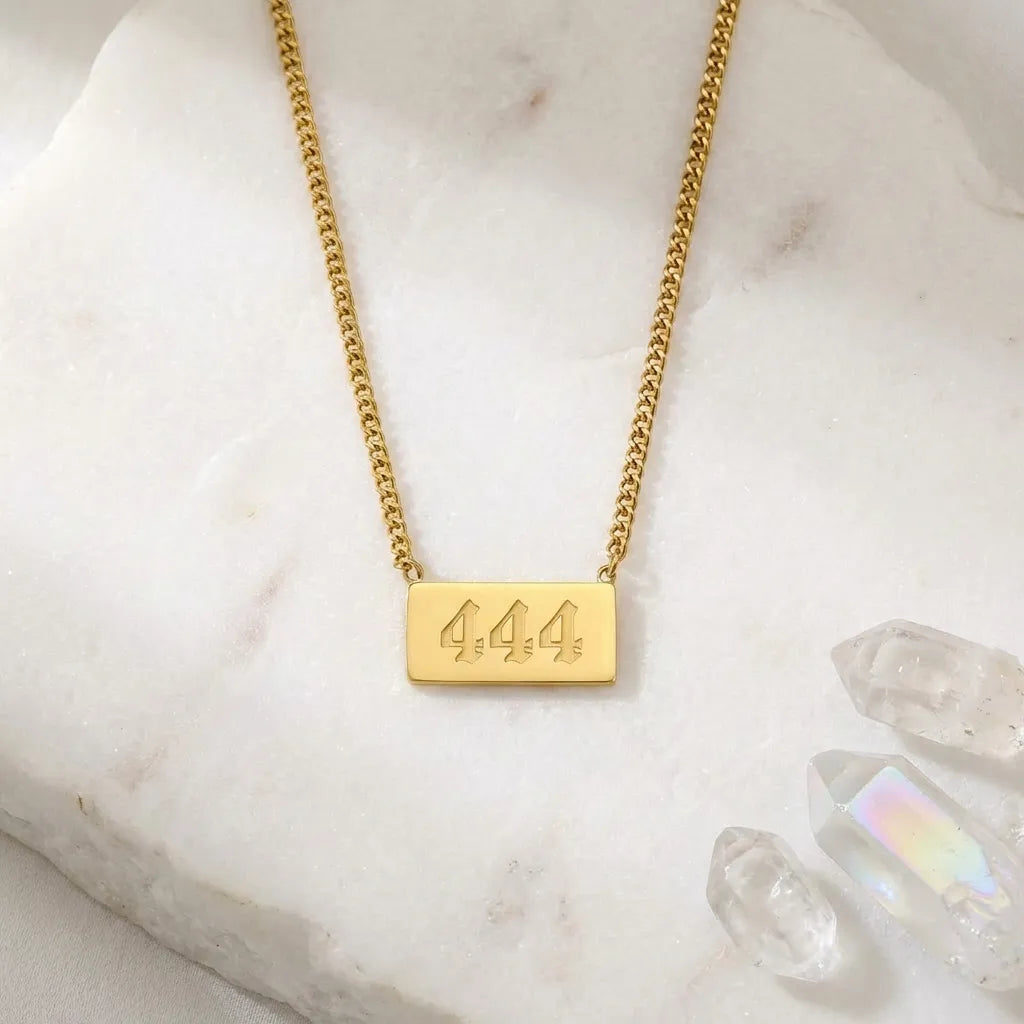 Gold necklace with a rectangular pendant displaying '444' on a marble surface.