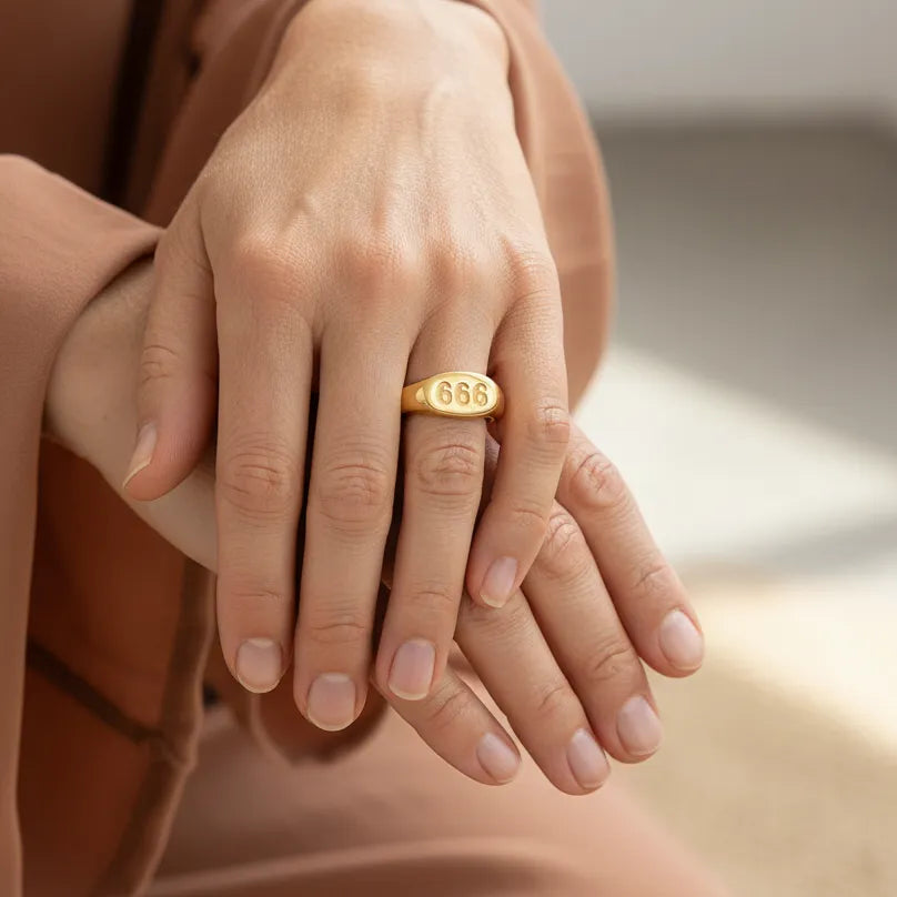 A close-up of a person's hands resting together, wearing a polished gold 666 ring