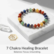 Colorful 7 Chakra Healing Bracelet on a white marble surface with a gold symbol and text.