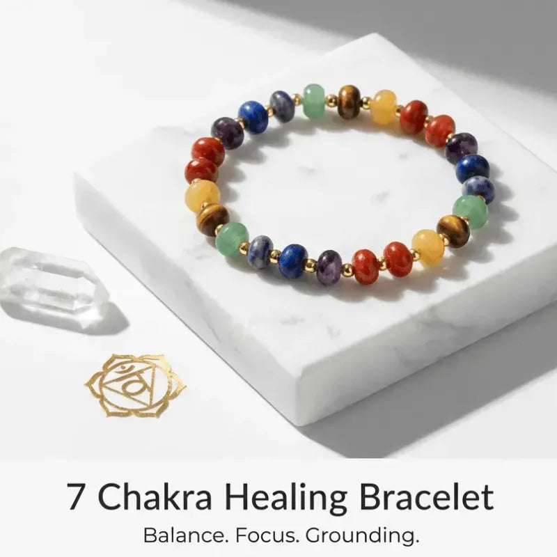 Colorful 7 Chakra Healing Bracelet on a white marble surface with a gold symbol and text.