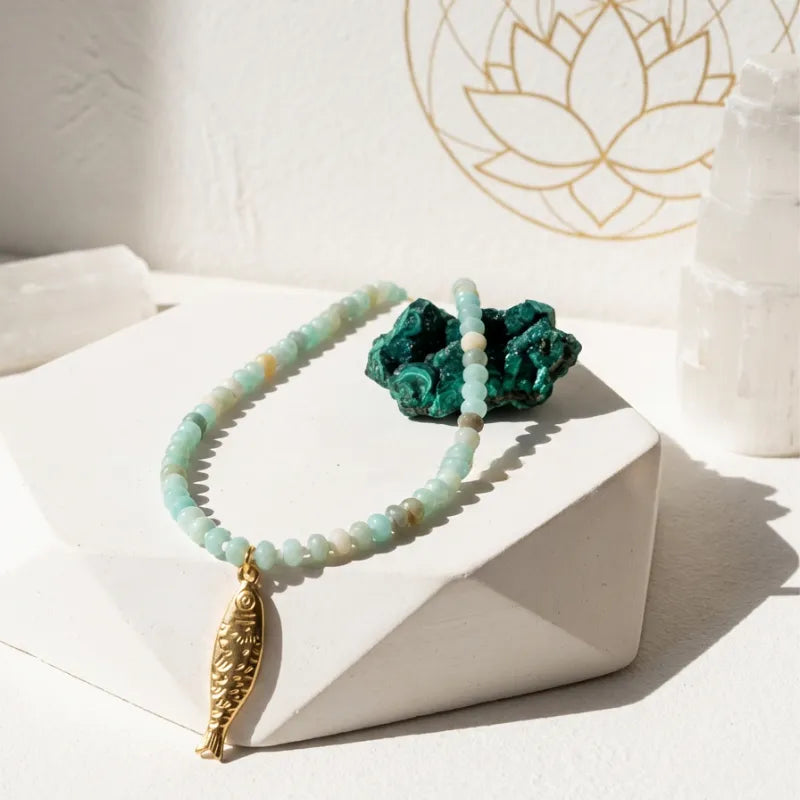 Necklace with gold fish pendant on a white surface with decorative elements