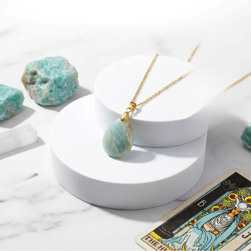 Gold necklace with a green pendant on a white surface with tarot card and crystals.