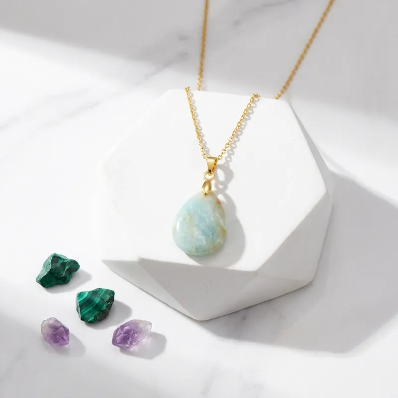 Necklace with a green pendant on a white surface with crystals.