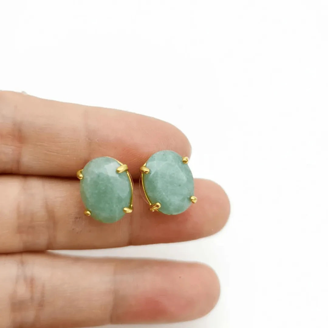 Green earrings with gold accents held between fingers on a white background