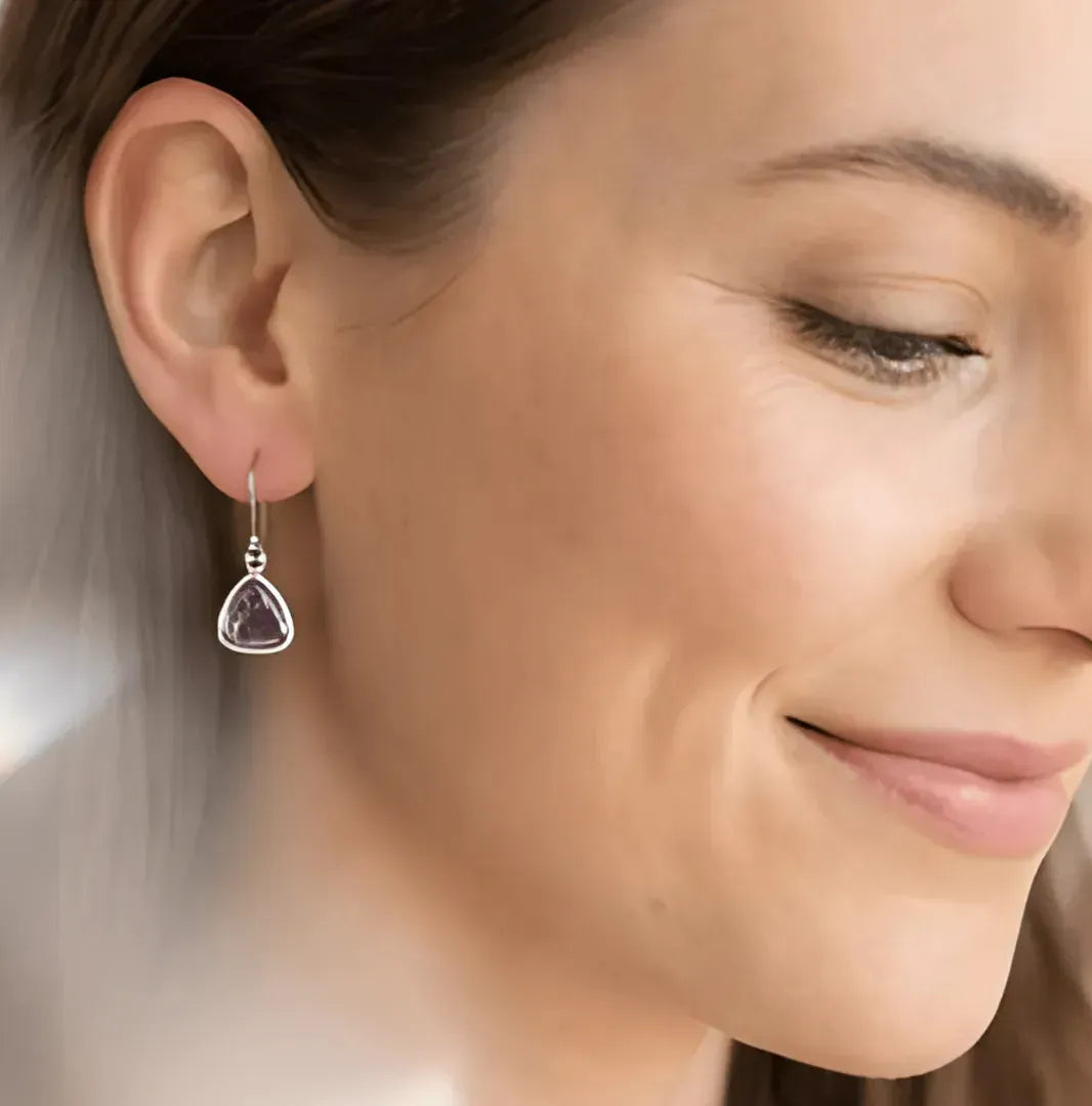 Gold earrings with purple gemstones on a light surface with crystals and plants.