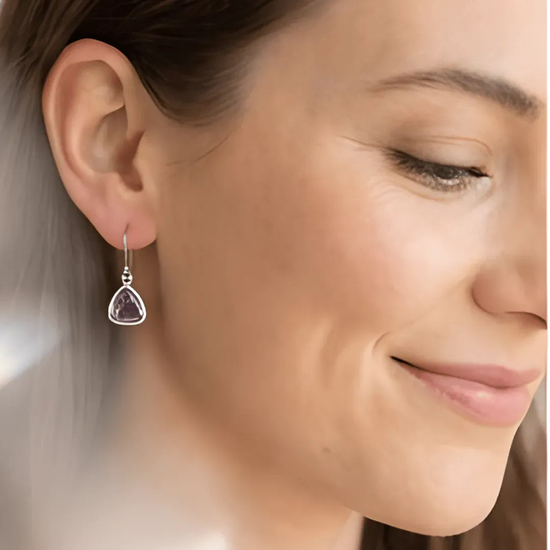 Gold earrings with purple gemstones on a light surface with crystals and plants.