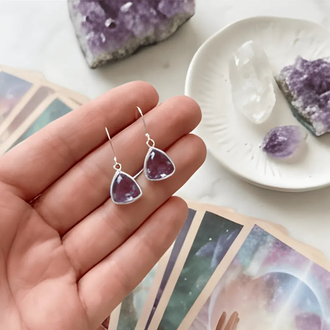 Purple teardrop earrings held in a hand with tarot cards and crystals in the background