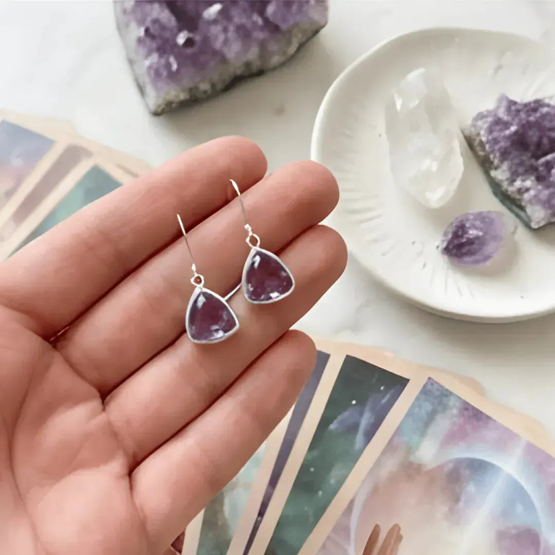 Purple teardrop earrings held in a hand with tarot cards and crystals in the background