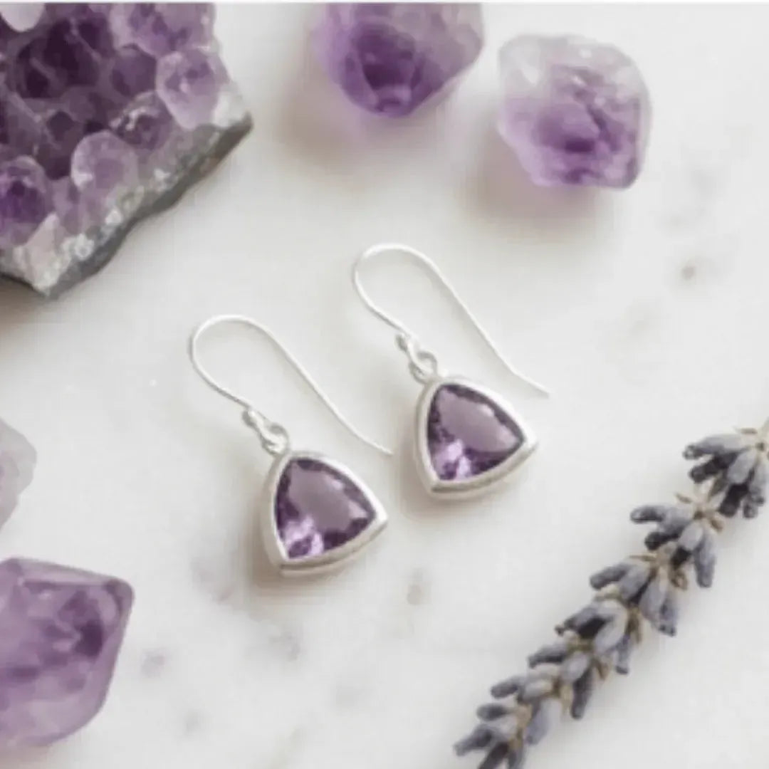Amethyst heart-shaped earrings on a marble surface with amethyst stones and lavender.
