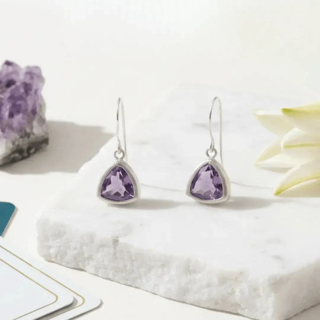 Pair of silver earrings with purple gemstones on a white surface.