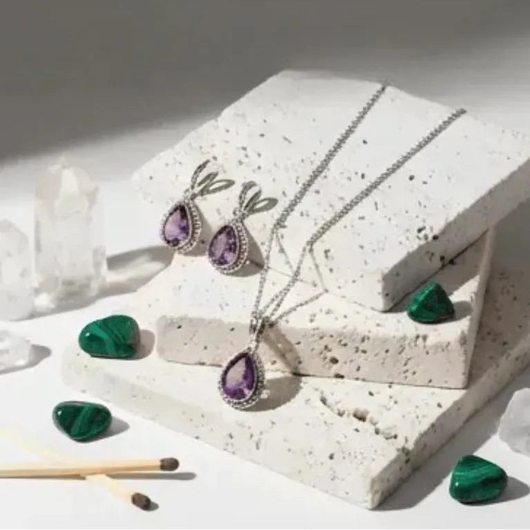 Jewelry set with amethyst and green gemstones on a textured white surface.