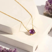 Gold necklace with a purple gemstone on a white surface with amethysts.