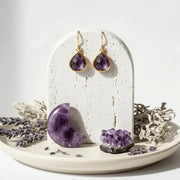 Amethyst earrings on a white stand with amethyst crystal and lavender flowers on a white background
