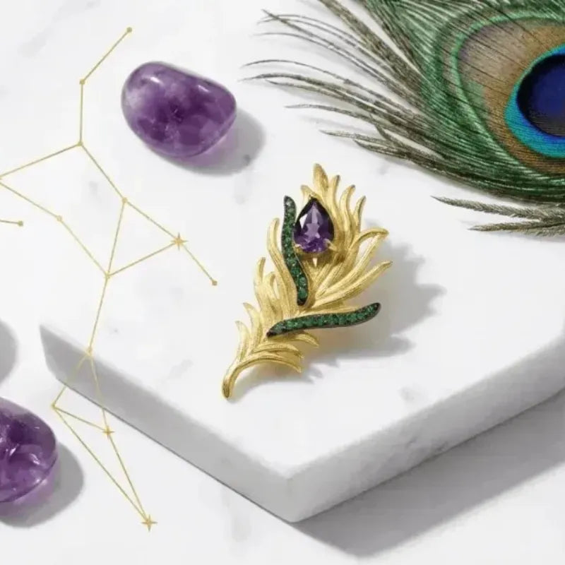 Gold feather-shaped brooch with gemstones on a white surface with amethysts and a peacock feather.