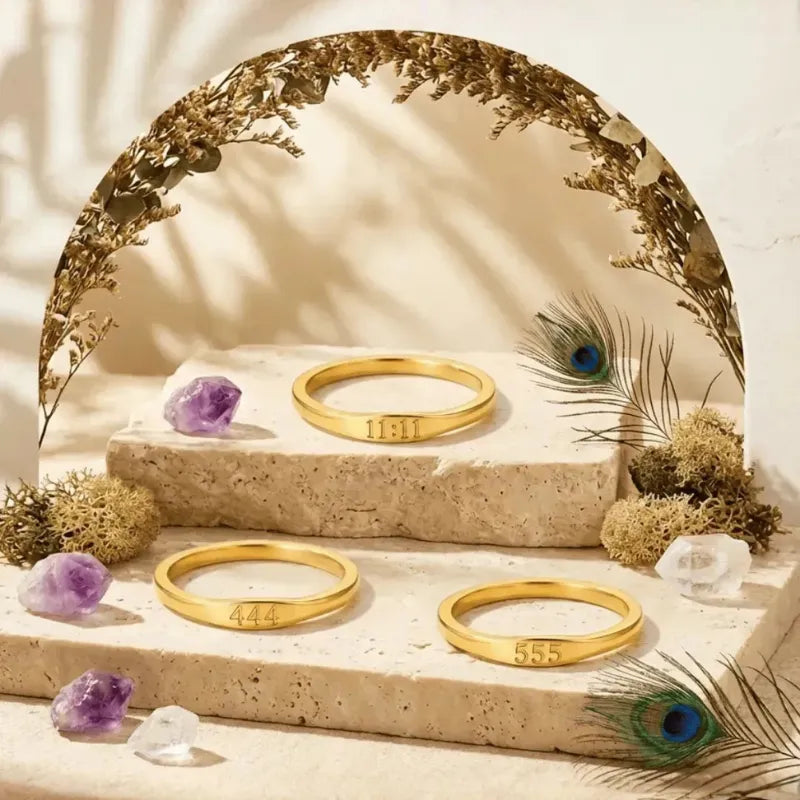 Three gold bracelets on a stone surface with decorative elements like peacock feathers and crystals.