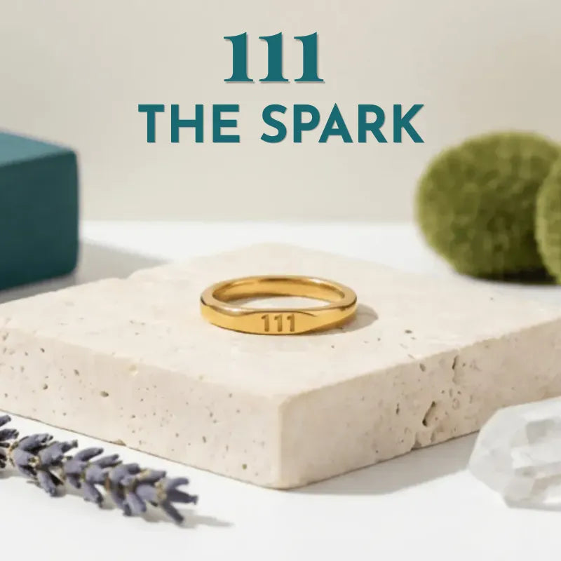 Gold ring with '111' on a beige stone surface with 'THE SPARK' branding.