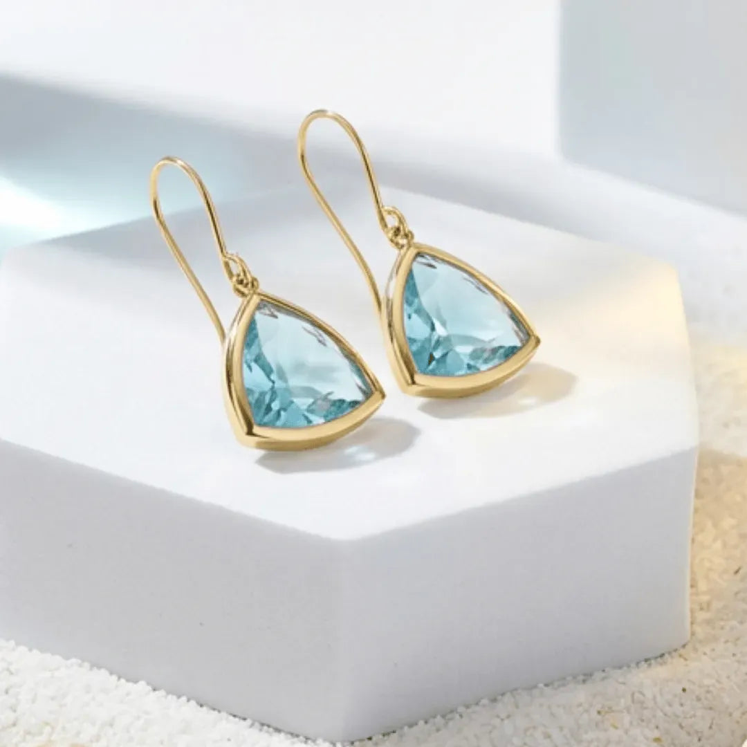 Gold earrings with blue gemstones on a white surface