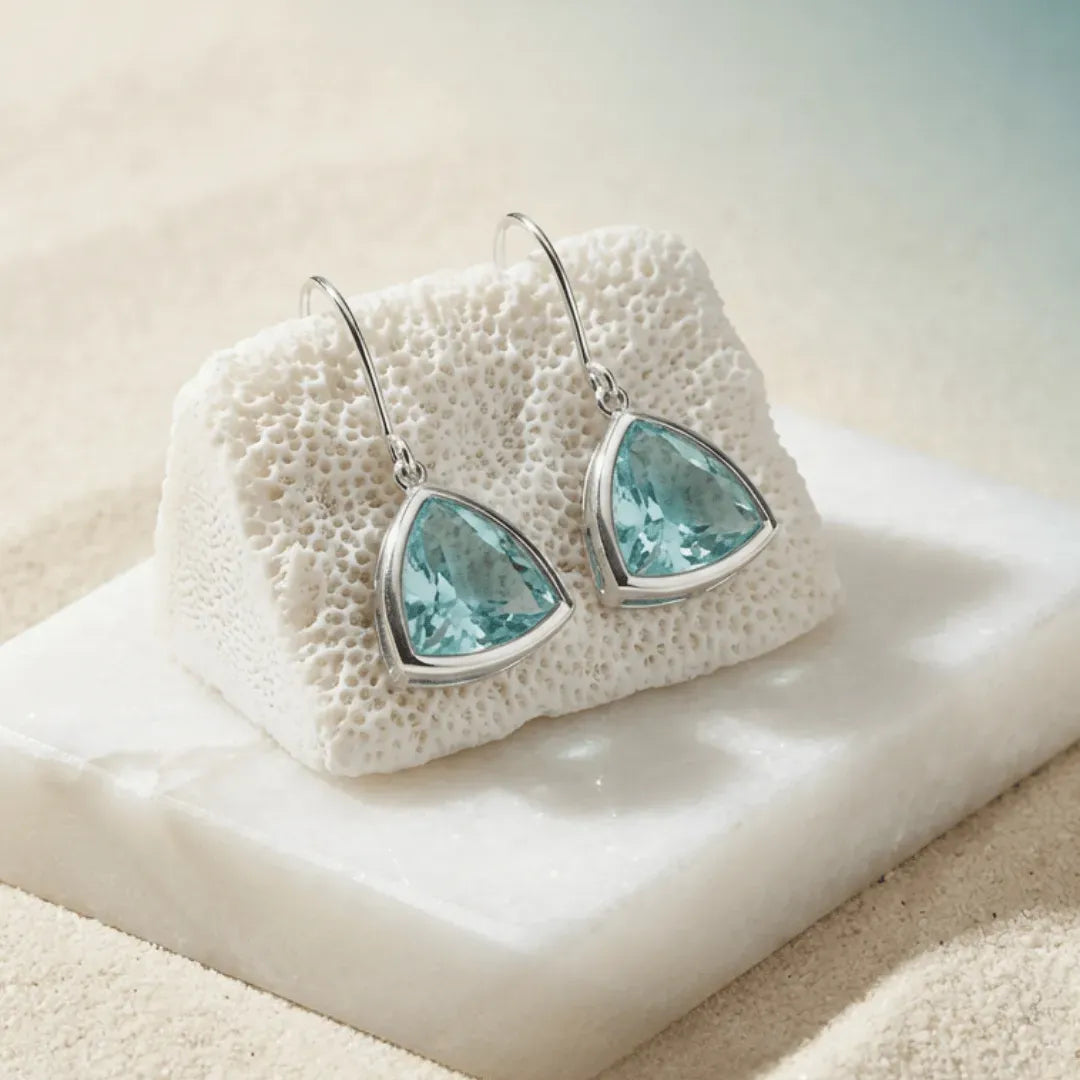 Teardrop-shaped earrings with blue gemstones on a textured white surface