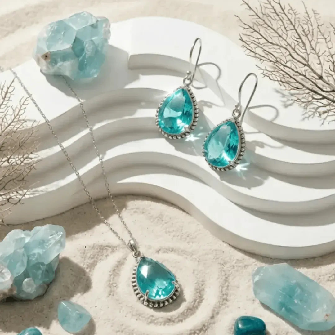 Turquoise teardrop jewelry set with silver accents on a sandy background