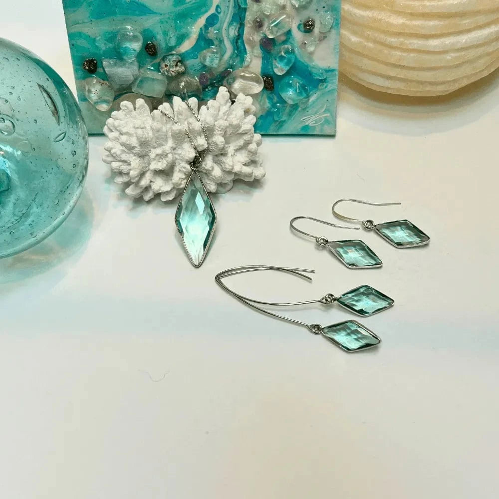 Turquoise earrings with silver hooks on a white surface with decorative items.