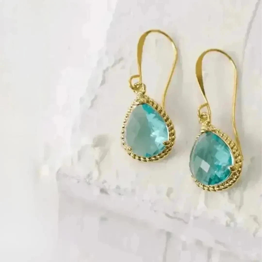 Gold earrings with turquoise stones on a white marble background