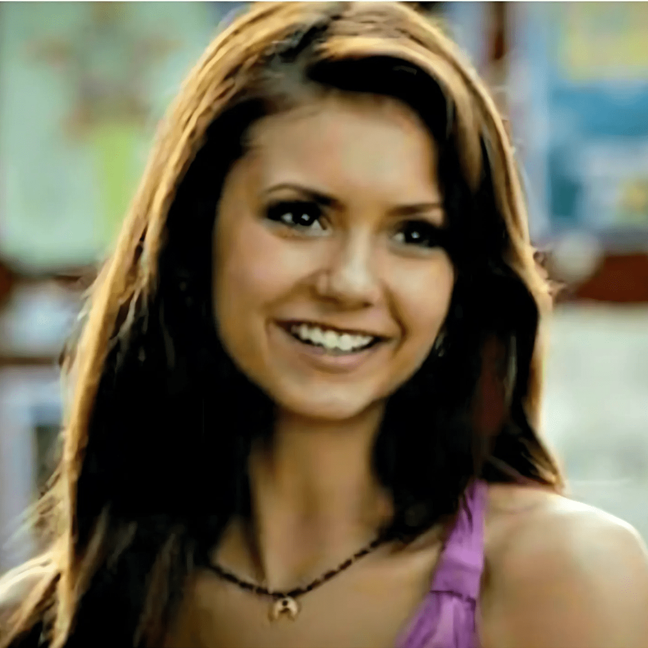 Woman with long brown hair smiling in a blurred indoor setting
