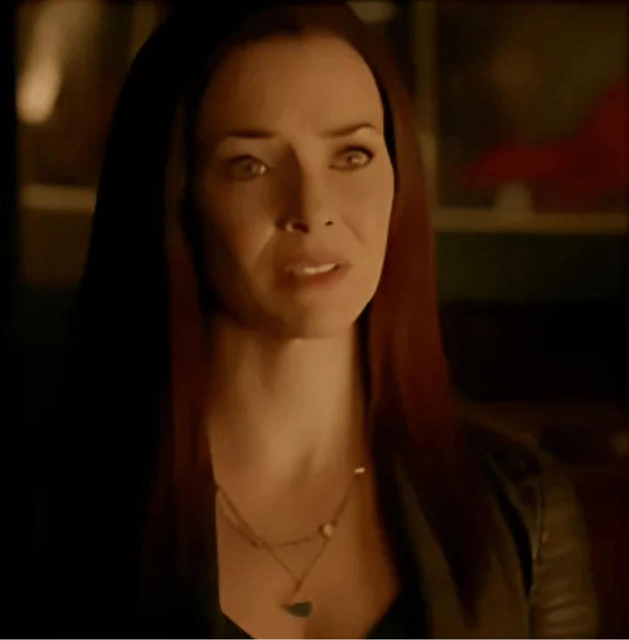 Woman with long hair wearing layered necklaces in a dimly lit setting
