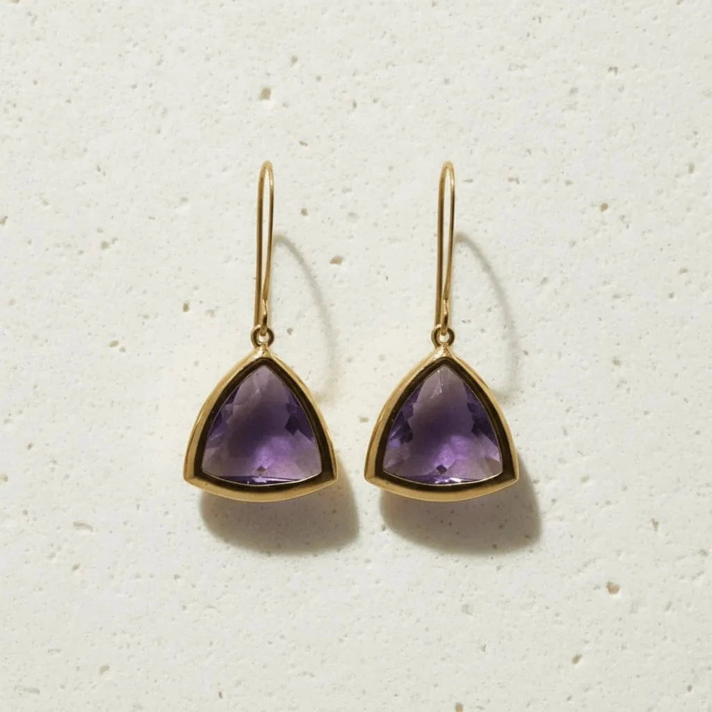 Gold earrings with purple gemstones on a textured white background