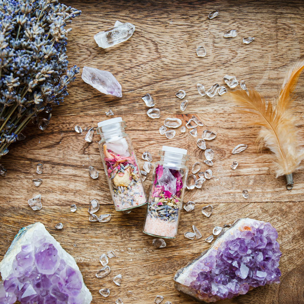 Two small glass bottles with colorful contents on a wooden surface with crystals and a feather.