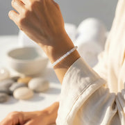 Person wearing a white bracelet with a blurred natural background