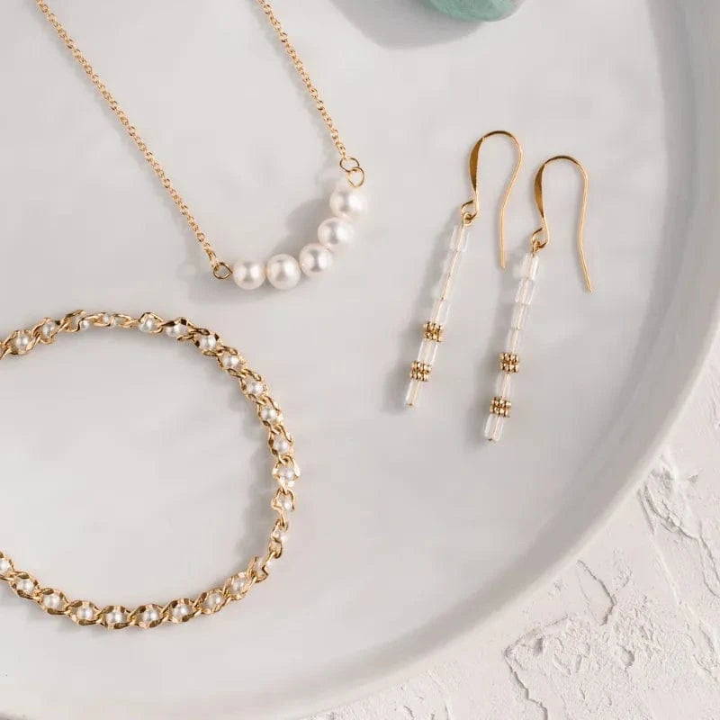 Gold jewelry set with necklace, bracelet, and earrings on a white plate.