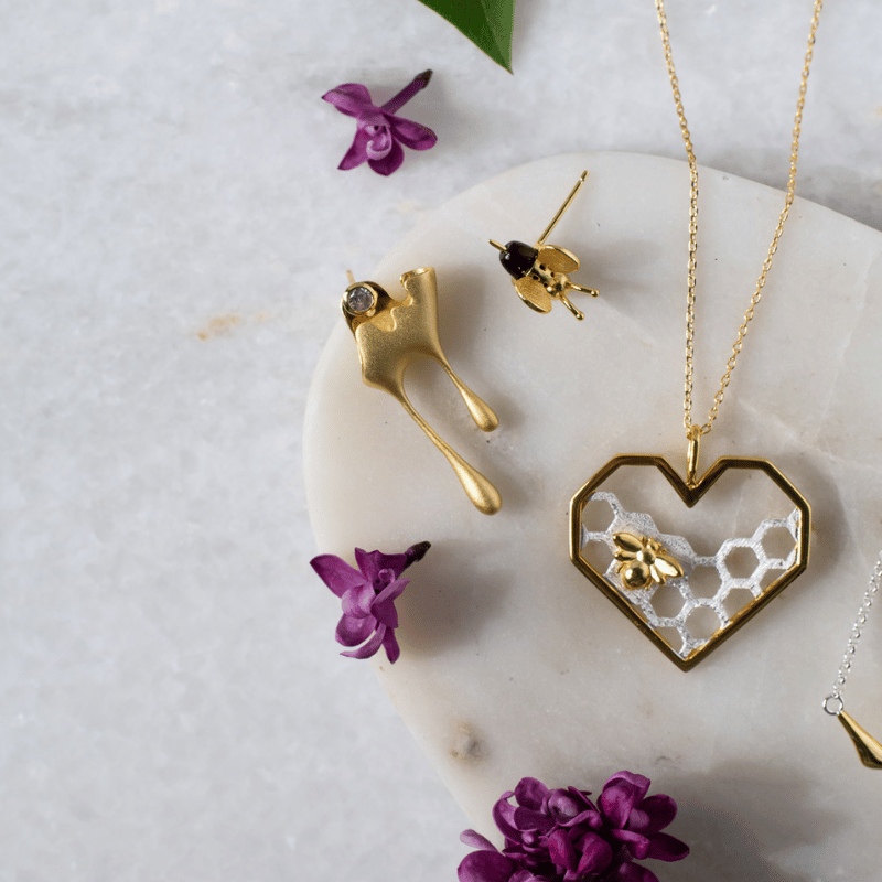 Gold jewelry set with heart-shaped pendant and earrings on a marble surface with purple flowers.