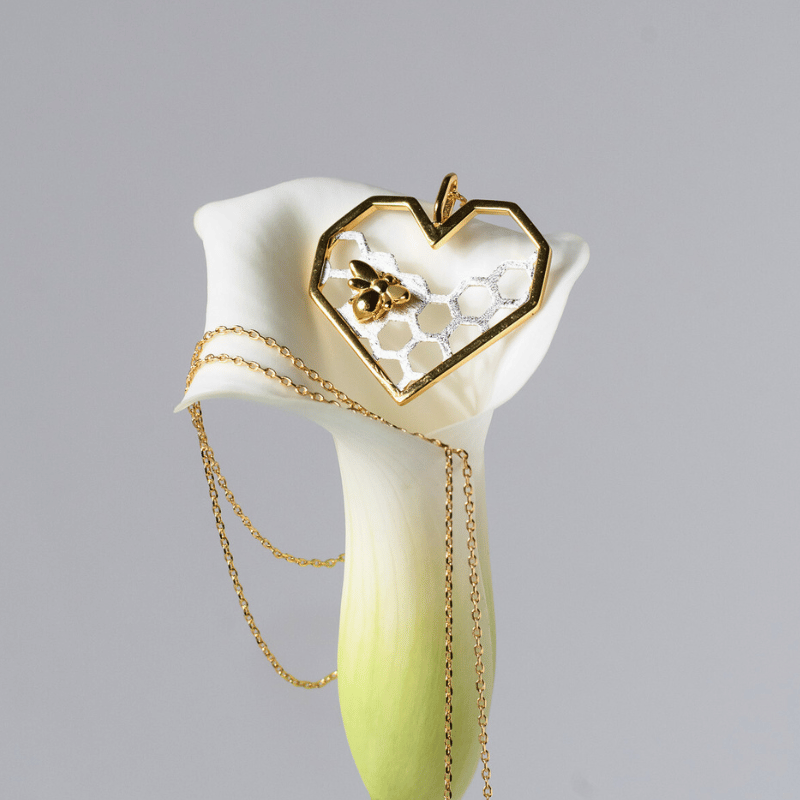 Heart-shaped pendant with gold chain on a white flower against a gray background