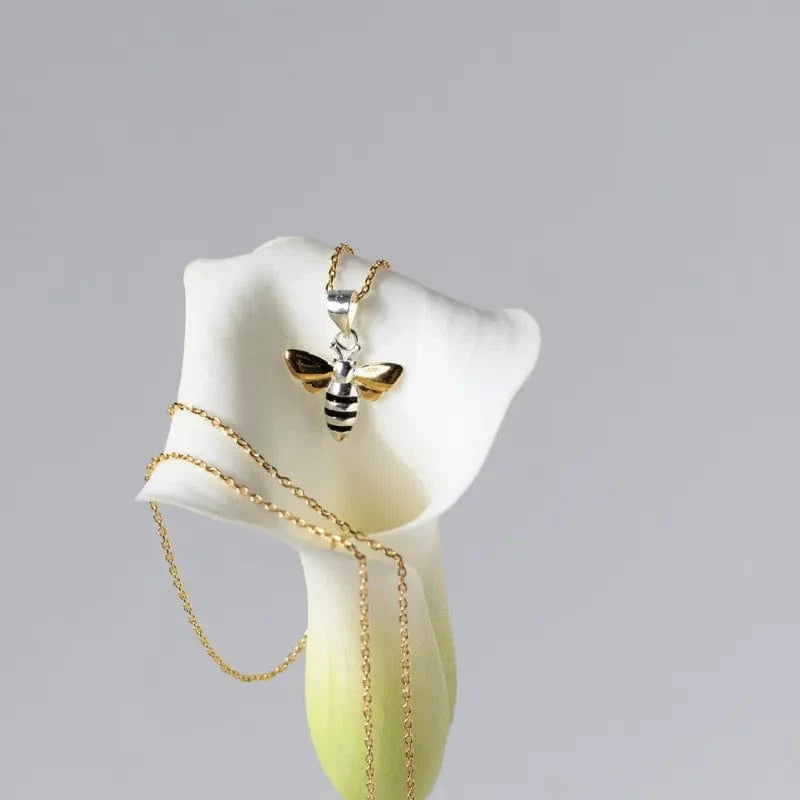 Gold necklace with a bee pendant on a white calla lily against a gray background