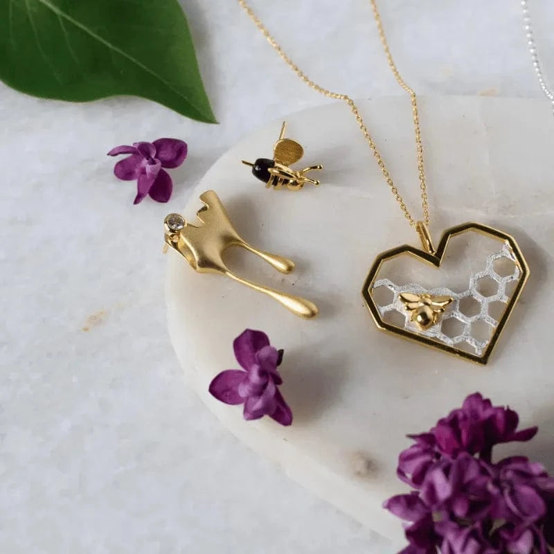 Gold necklace with heart and honeycomb design on a marble surface with purple flowers.