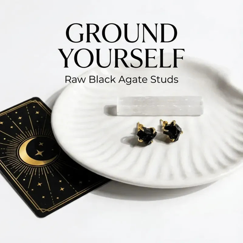 Black agate stud earrings on a white plate with a tarot card and crystal, against a white background.