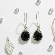 Black teardrop earrings with silver hooks on a light gray background