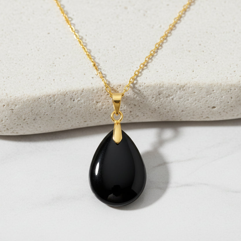 Gold necklace with a black teardrop pendant on a white background