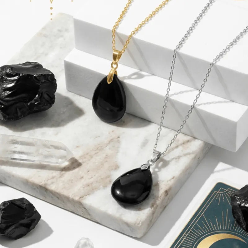 Black teardrop pendants on gold and silver chains with crystals on a marble surface.