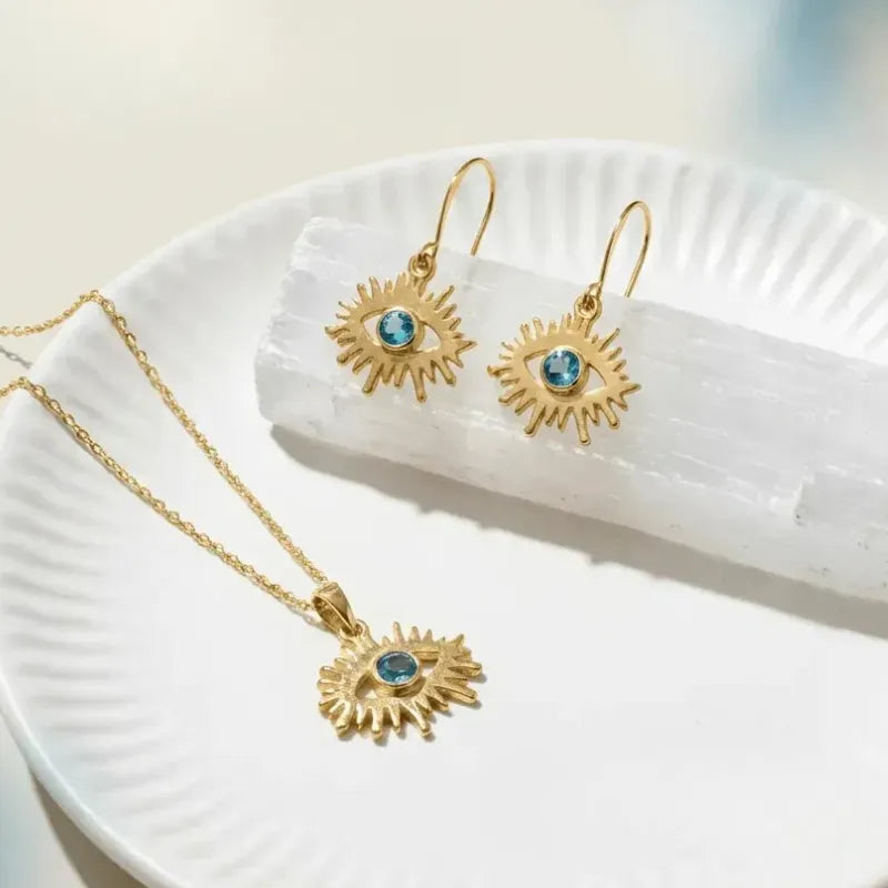 Gold jewelry set with sun-shaped earrings and necklace on a white plate